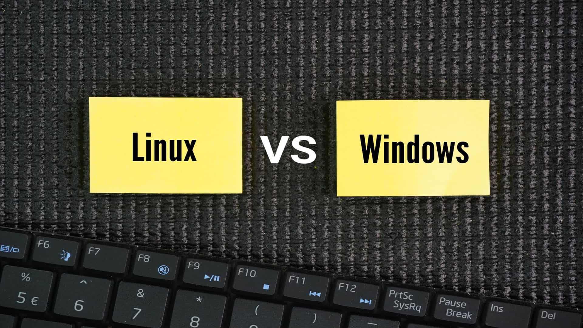 Cartões amarelos sobre um fundo escuro exibem as palavras Linux e Windows com a sigla VS no centro enquanto parte de um teclado aparece na parte inferior