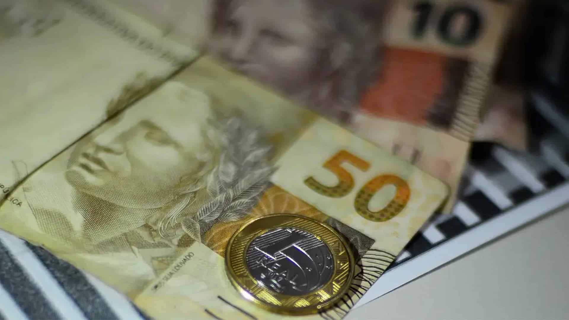 Notas e moeda de Real colocadas uma sobre as outras