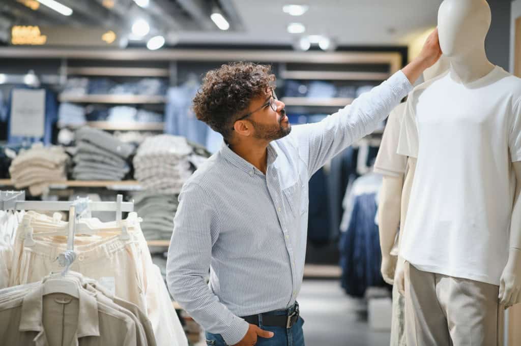 Homem olhando para cima e colocando a mão na roupa que está em um manequim