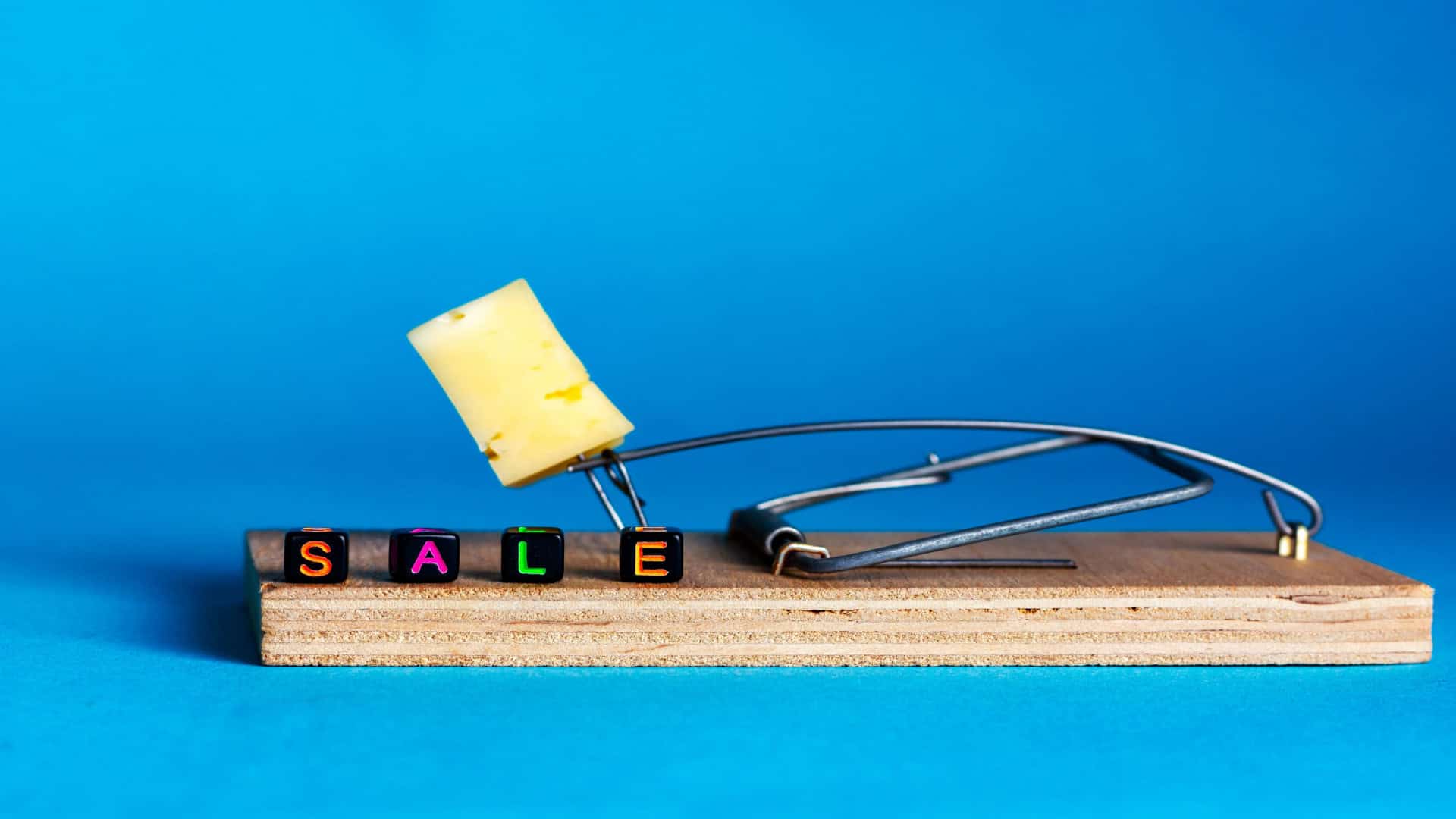 Ratoeira com um pedaço de queijo e cubos coloridos formando a palavra “SALE” sobre fundo azul, simbolizando armadilhas de promoções falsas na Black Friday