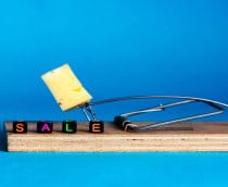 Ratoeira com um pedaço de queijo e cubos coloridos formando a palavra “SALE” sobre fundo azul, simbolizando armadilhas de promoções falsas na Black Friday