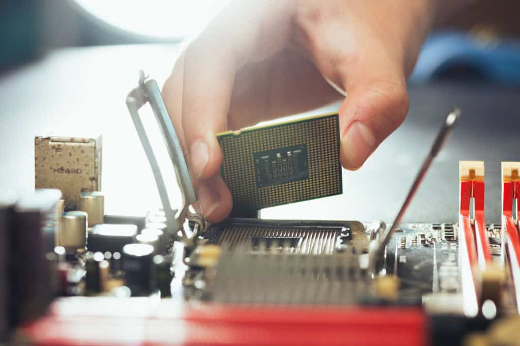 Mão instalando um processador no soquete da placa-mãe de um PC, representando o processo de atualização de hardware e a importância da compatibilidade entre os componentes