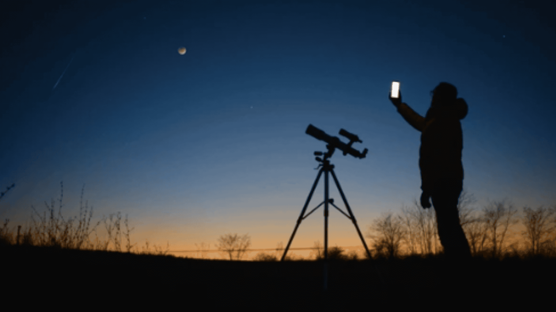 pessoa tirando foto da lua com o celular, com o céu anoitecendo, em um local aberto e um telescópio do lado.