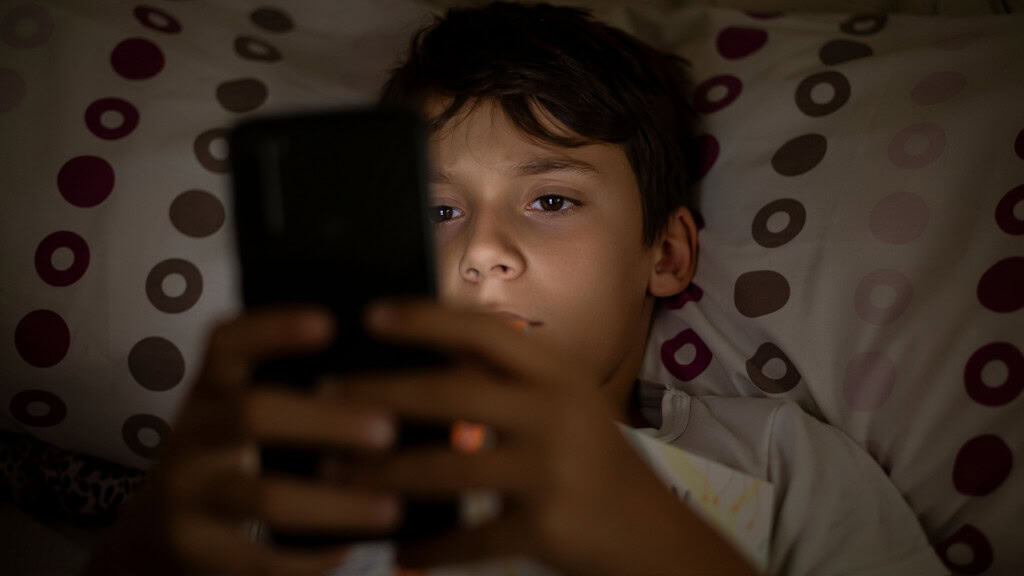 Menino usando celular deitado na cama