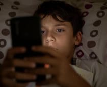 Menino usando celular deitado na cama