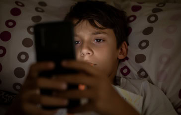 Menino usando celular deitado na cama