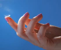 Lente de contato no dedo contra o céu azul para a boa visão sem óculos e cuidados modernos do olho