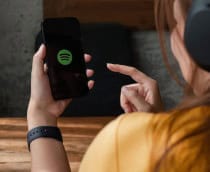 Jovem de costas com fones mexendo no app Spotify em um celular.