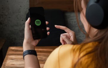 Jovem de costas com fones mexendo no app Spotify em um celular.