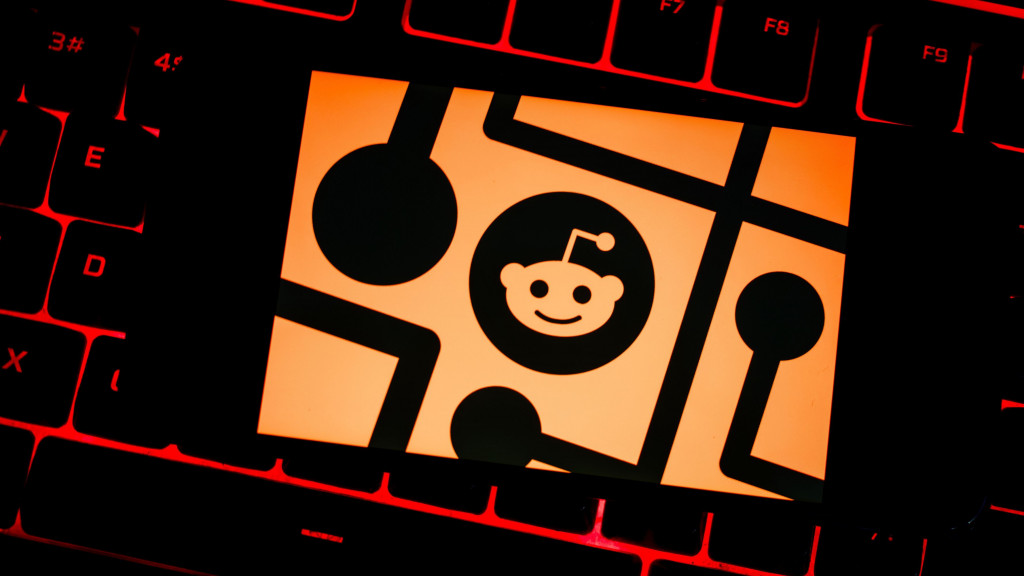 Ilustração com logomarca do Reddit em cima de teclado de notebook com teclas com retroiluminação vermelha acesa