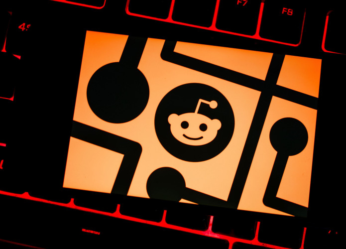 Ilustração com logomarca do Reddit em cima de teclado de notebook com teclas com retroiluminação vermelha acesa