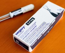 Caneta do Wegovy ao lado de caixa do medicamento; ambos estão em cima de uma mesa de madeira