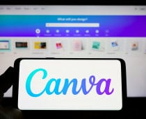 Ao fundo, desfocado, o site do Canva em um monitor; à frente, um smartphone na horizontal com o logo da plataforma