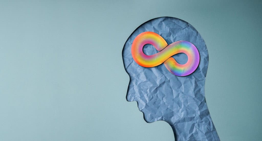 Silhueta de uma cabeça em papel amassado com o símbolo do infinito colorido na área do cérebro, sugerindo a ideia de que o autismo não é doença nem transtorno psicológico, mas uma forma diferente de neurodesenvolvimento.