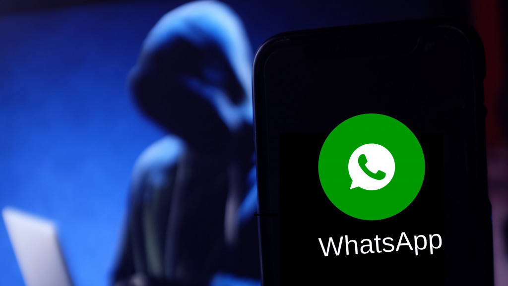 Celular com ícone do WhatsApp na tela; ao fundo, um hacker encapuzado usando um notebook
