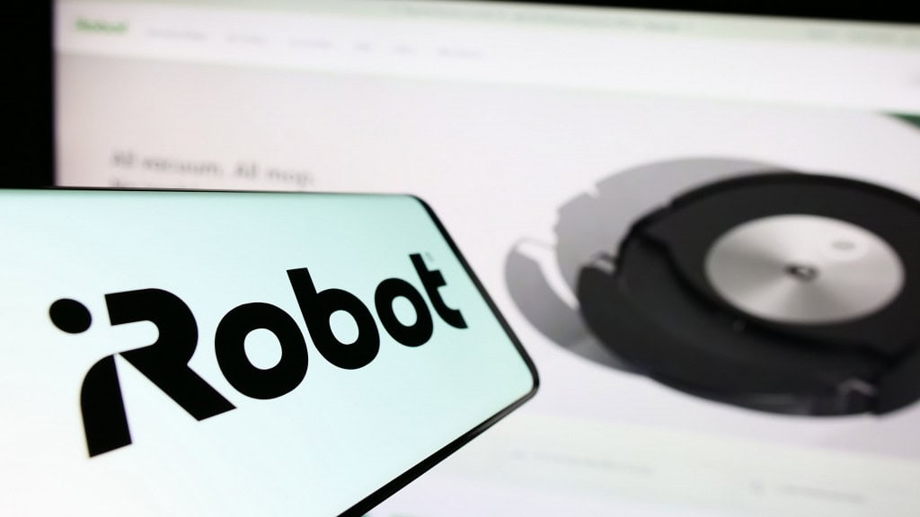 Celular com logomarca da iRobot na tela colocado na frente de monitor exibindo página do Roomba, aspirador robô da marca