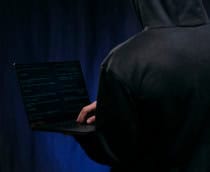 homem de costas usa agasalho escuro cobrindo a cabeça e segura notebook