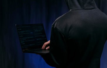 homem de costas usa agasalho escuro cobrindo a cabeça e segura notebook