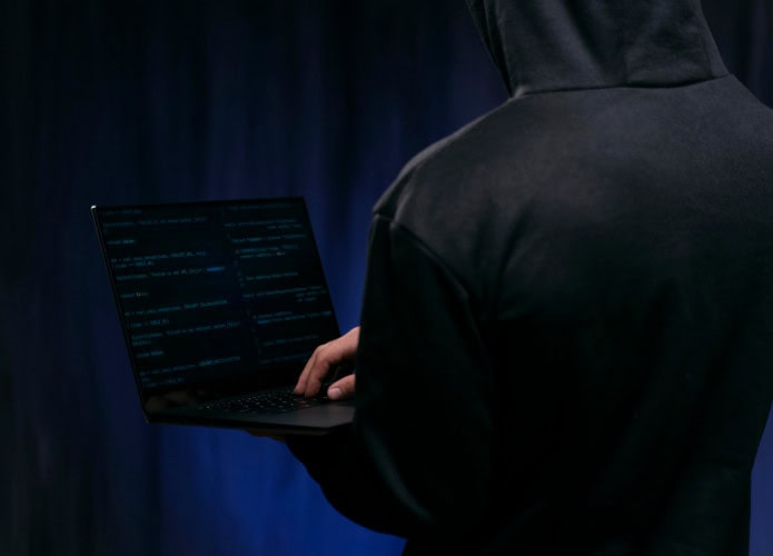 homem de costas usa agasalho escuro cobrindo a cabeça e segura notebook