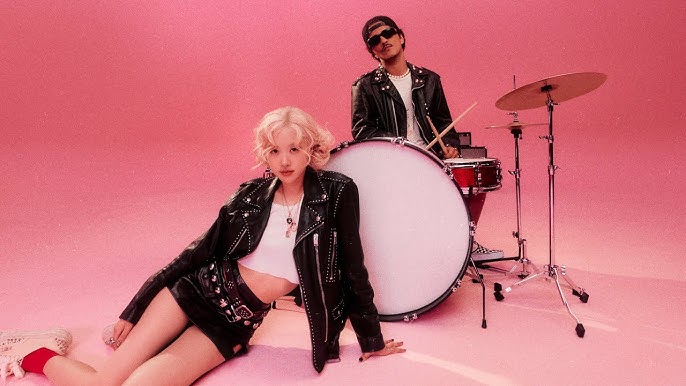 Os artistas Rosé (apoiada no chão) e Bruno Mars (atrás dela, tocando bateria)