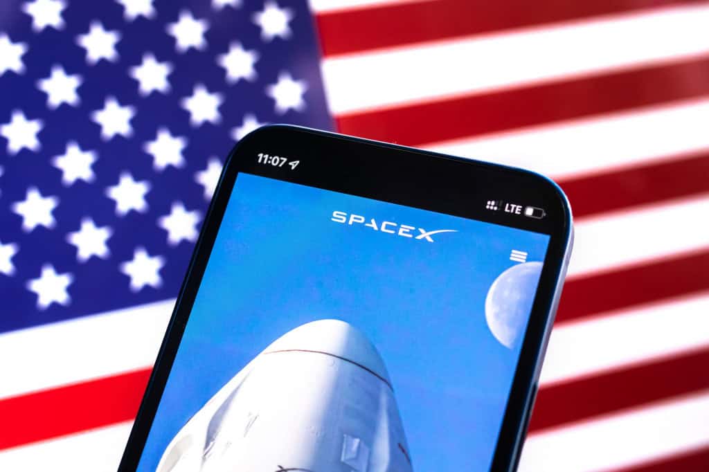 Ao fundo, bandeira dos EUA; à frente, página da SpaceX em um smartphone