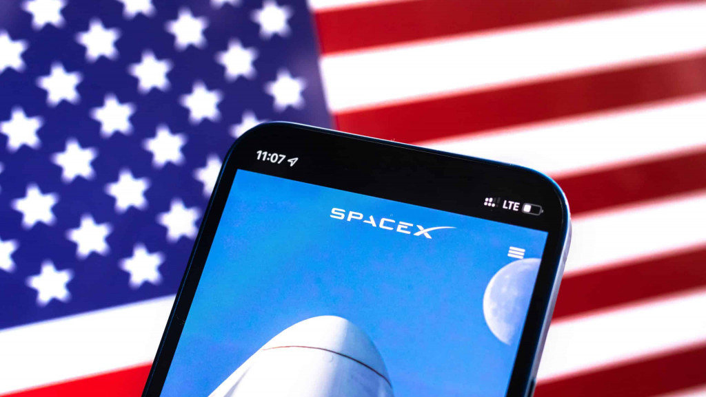 Ao fundo, bandeira dos EUA; à frente, página da SpaceX em um smartphone
