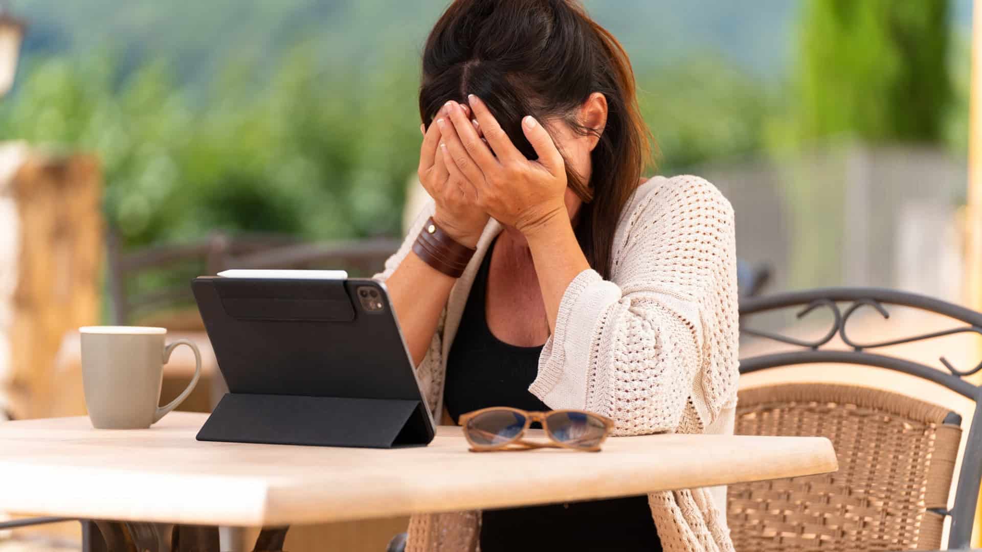 mulher em frente a um tablet com as mãos no rosto