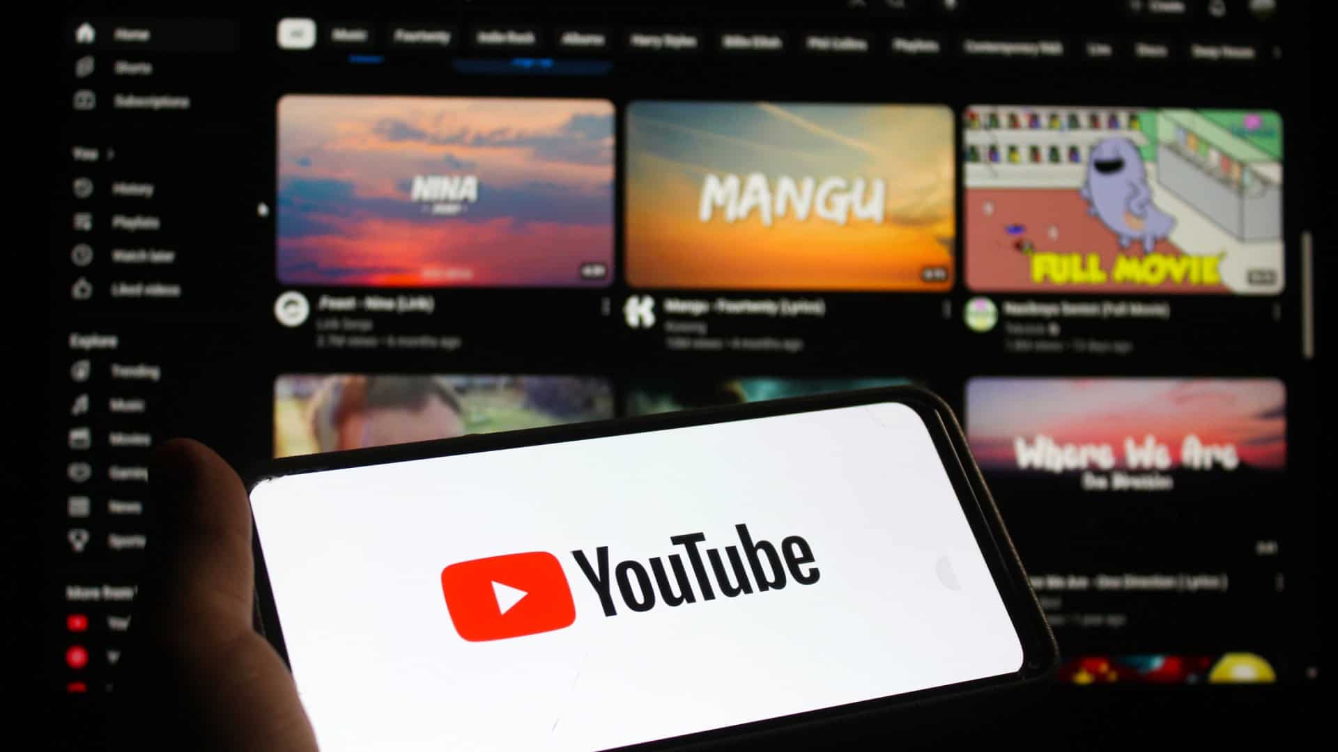 Ao fundo, página web do YouTube; à frente, logo do YouTube em um smartphone na horizontal