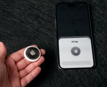 Pessoa com AirTag na mão ao lado de iPhone