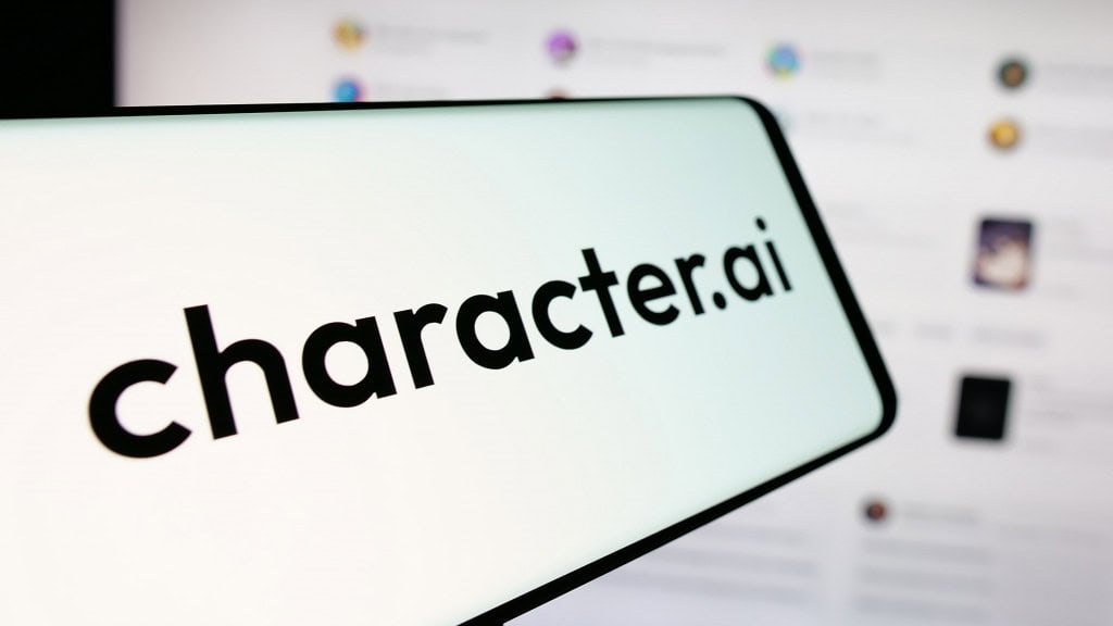 Celular com logomarca da Character.AI na tela; aparelho está na frente de monitor exibindo tela da plataforma