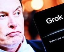 Celular mostrando logomarca do Grok; ao fundo, um monitor exibe uma foto de Elon Musk como se ele olhasse para o aparelho