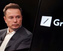 Celular mostrando ícone do Grok; aparelho está na frente de tela maior mostrando foto de Elon Musk