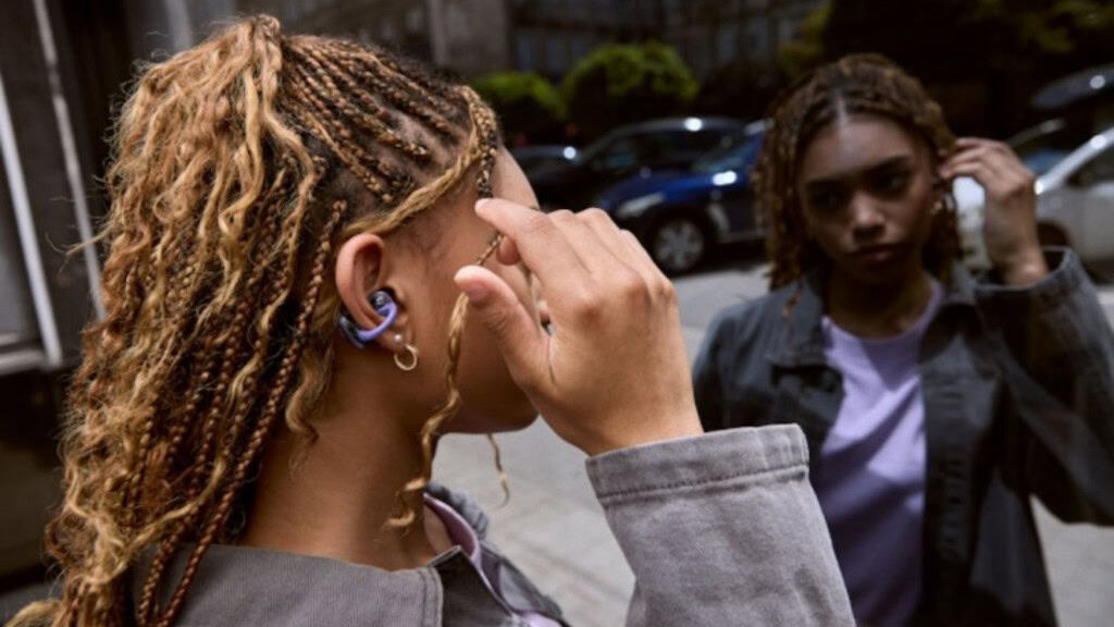 Mulher usando fone da JBL e olhando para o próprio reflexo em janela