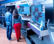 Pessoas de costas olhando para várias TVs à venda