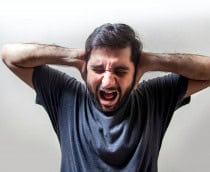 homem num ambiente com fundo neutro, com ambas as mãos prensadas no ouvido, gritando com todas as forças