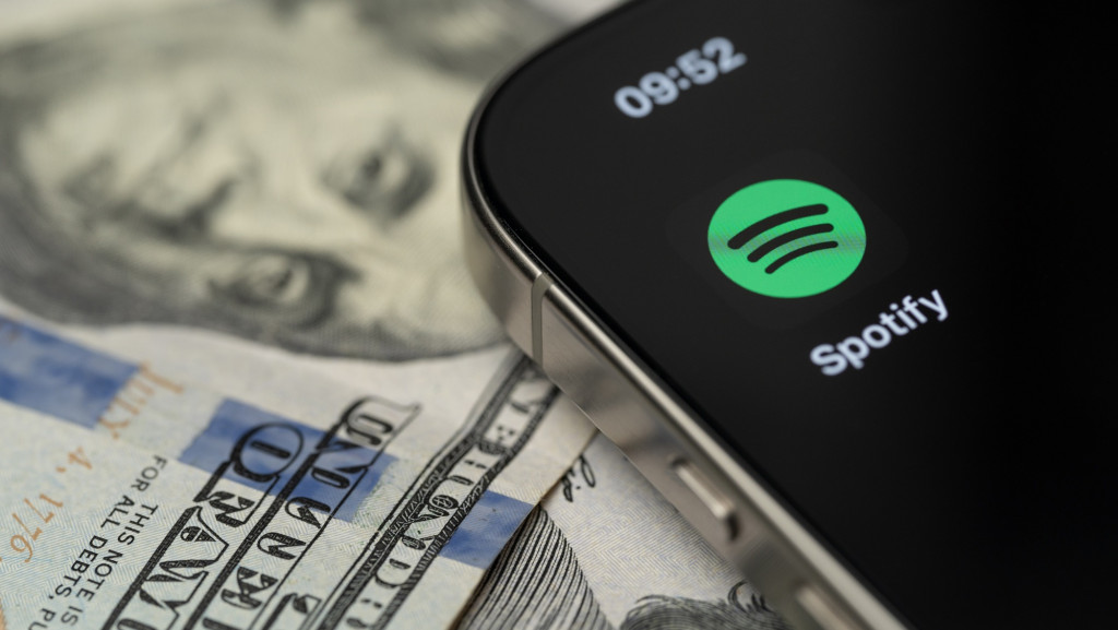 Logo do Spotify em um smartphone; abaixo dele, notas de dólar