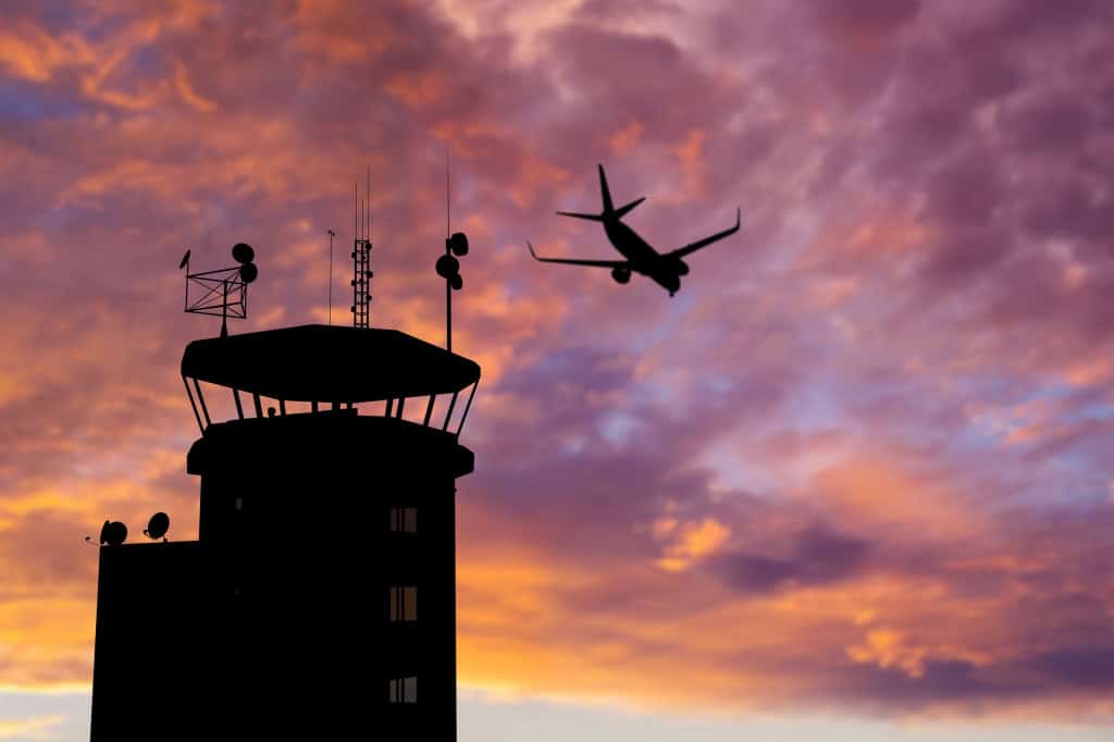 Uma torre de controle em um aeroporto em contraste com um avião no ar