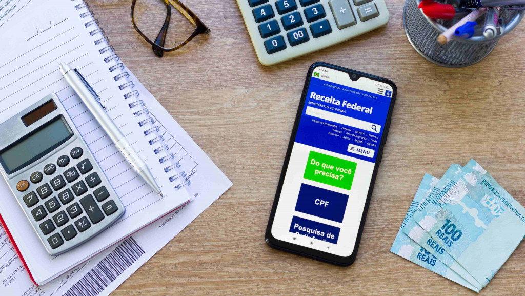 Mesa com calculadora e celular aberto no app da Receita Federal para calcular o imposto de renda (IR)