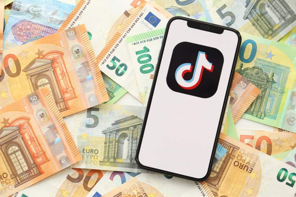 Smartphone com o logo do TikTok exibido na tela e em cima de notas de dinheiro