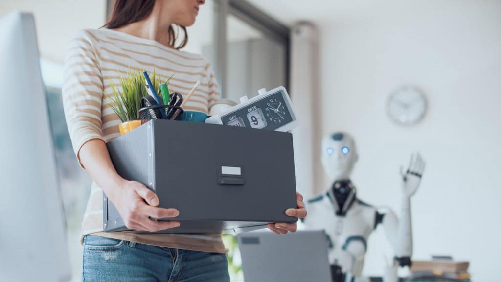 Mulher demitida carregando caixa para fora do escritório enquanto robô com inteligência artificial acena no fundo