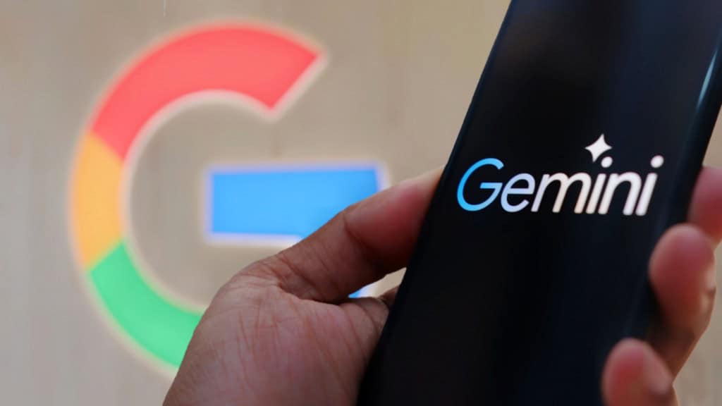Pessoa segurando celular com logomarca do Gemini na tela; ao fundo, aparece o logotipo do Google