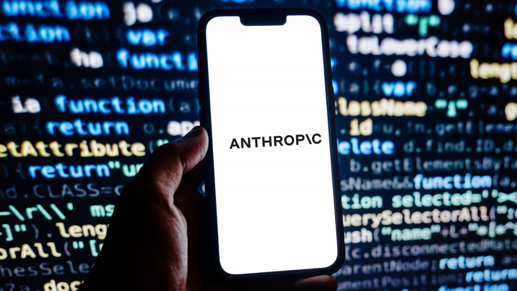 Logo da Anthropic em um smartphone; ao fundo, várias linhas de código de programação