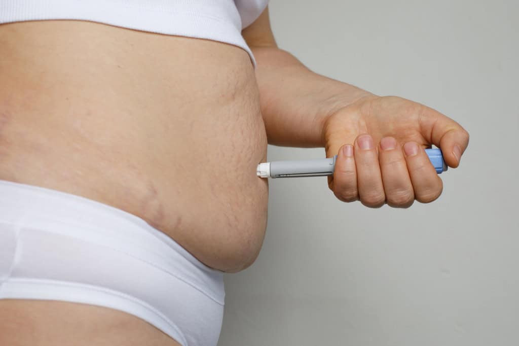 Pessoa aplicando uma caneta emagrecedora em sua barriga
