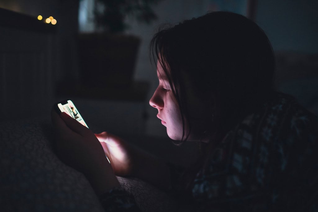 Criança no escuro usando um celular