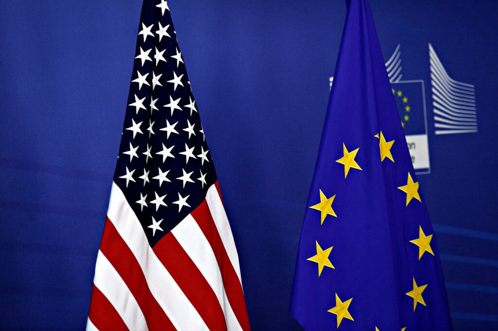 Bandeiras dos Estados Unidos e da União Europeia lado a lado em ambiente institucional