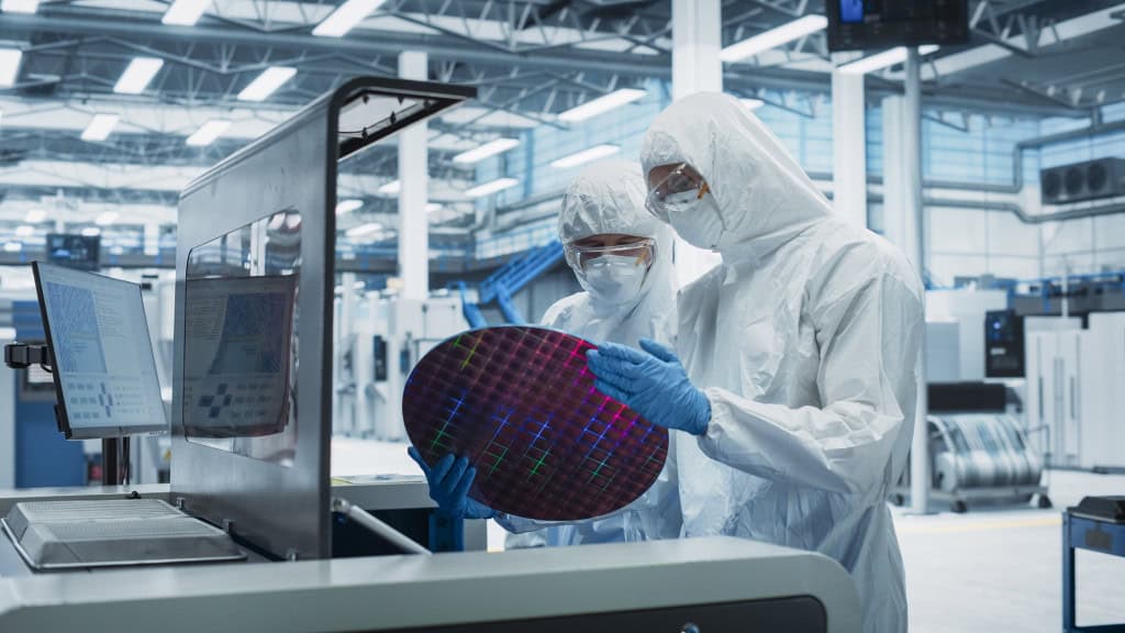 Engenheiros em ambiente controlado analisam wafer de silício em fábrica de semicondutores