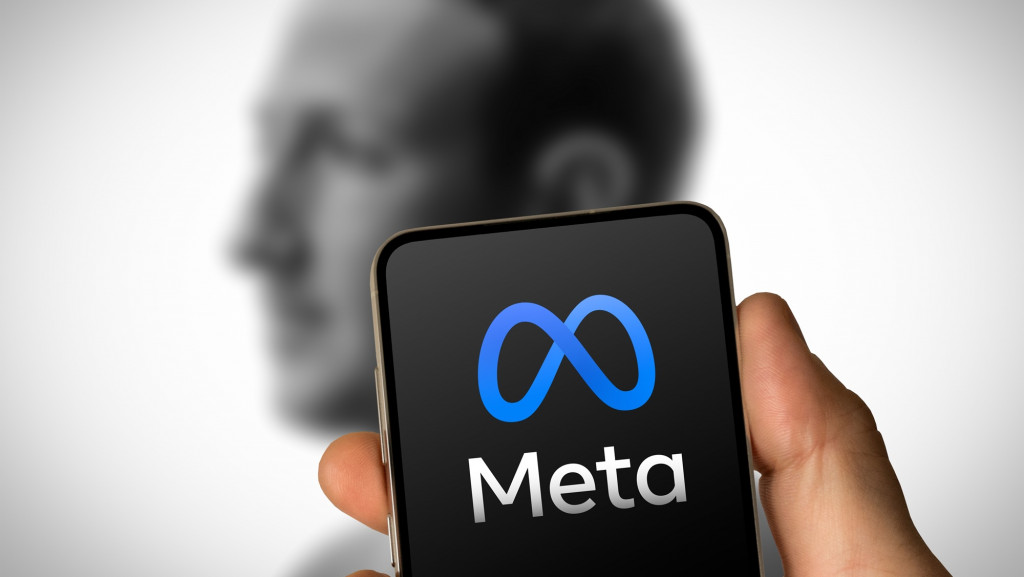 Logo da Meta exibido na tela de um smartphone, com silhueta desfocada de Mark Zuckerberg ao fundo