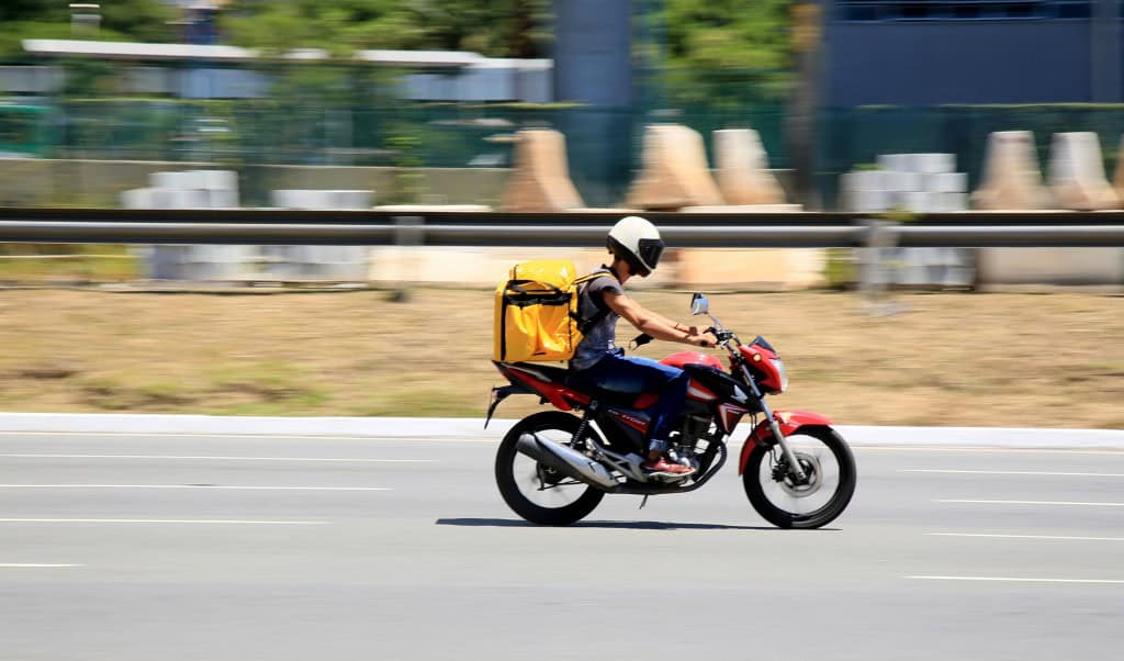 Motociclista andando de moto, com capacete e uma mochila de entregas
