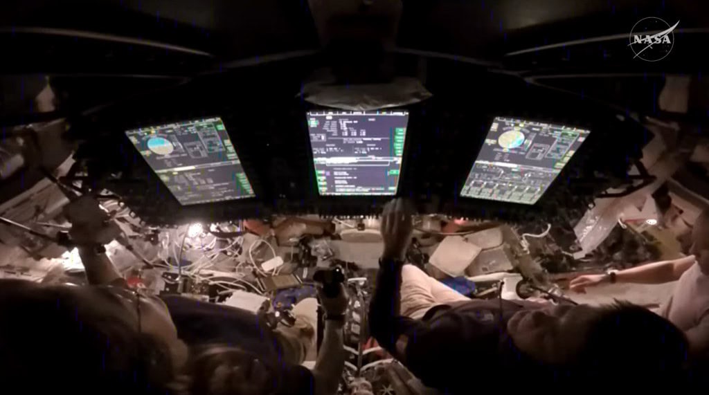 A astronauta da NASA Christina Koch, à esquerda, assume o controle da espaçonave Orion durante um teste de pilotagem manual no quarto dia de voo da missão Artemis II. À sua direita estão o astronauta da CSA (Agência Espacial Canadense) Jeremy Hansen e o astronauta da NASA Victor Glover.