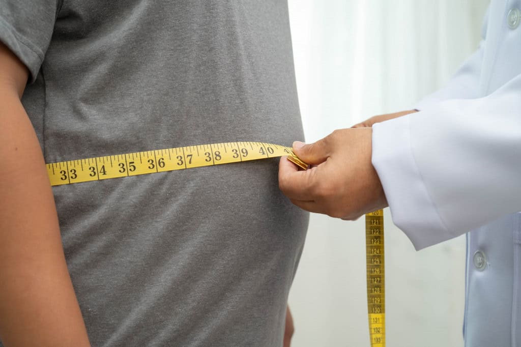 Pessoa segurando uma fita métrica ao redor da barriga de outra pessoa